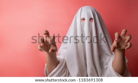 young child dressed in a ghost costume for halloween on pink background.