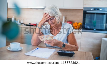 Stressed senior woman is doing banking and administrative work at home. Elderly woman looking at her utility bills and paperwork. Woman with documents in her hands makes up her personal budget