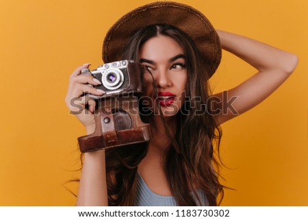Close-up photo of concentrated female photographer with dark long hair. Indoor portrait of cute girl wears brown hat.