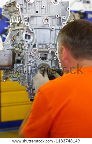 The mechanic in an orange T-shirt sets the gear to the engine of the car.