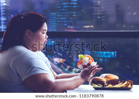 Picture of fat woman eating junk foods at night time while sitting in the restaurant