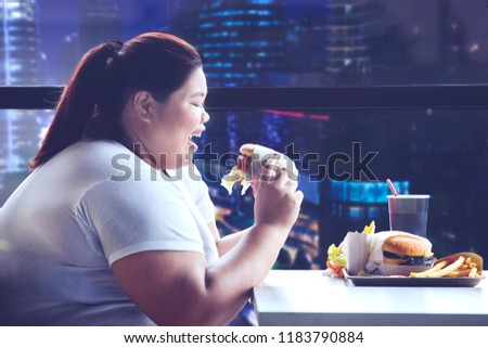 Picture of young obese woman having dinner with junk food in the restaurant