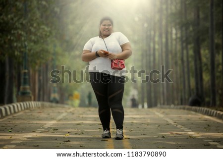 Picture of overweight woman smiling at the camera while holding a smartphone in the road