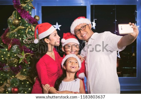 Portrait of happy family taking a selfie picture together by using a smartphone near a Christmas tree in the living room