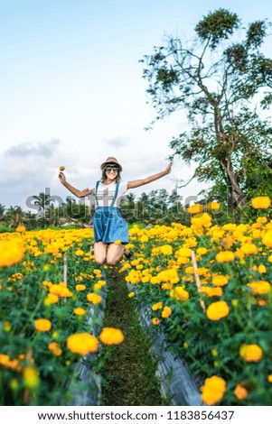 Close up portrait of happy and beautiful young woman relaxing enjoying the fresh beauty of gorgeous orange marigold flowers field in travel and holidays. Bali island.