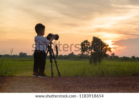 Cute asian boy learning to taking photo from DSLR Camera in his hand with nature outdoor background.