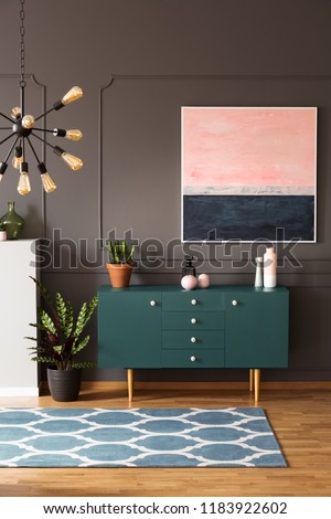 Real photo of moroccan trellis carpet placed on wooden floor in dark living room interior with green cupboard with decor, painting on wall and fresh plants Royalty-Free Stock Photo #1183922602
