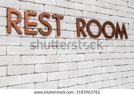 Metal copper gold color letters of REST ROOM on white brick wall  