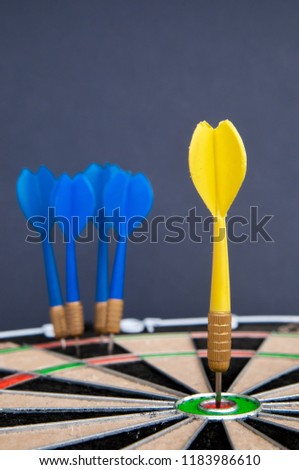 Close-up view of a yellow dart on the bullseye fand a group of blue darts all together in the background