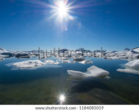 Floating Sea Ice in Ilulissat Icefjord with reflection of sunstar in a dramatic blue sky.Low angle view.Ice melt.Climate Crisis and Breakdown.Climate Emergency Image
