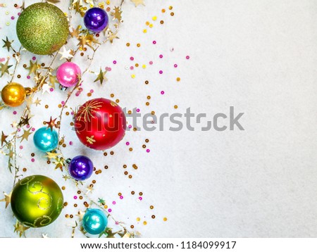 Multi-colored round Christmas tree toys of different sizes, twisted gold garland, colored confetti lie on a white textural background horizontally with copy space