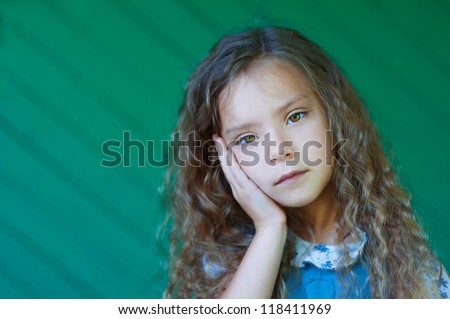 Portrait of beautiful sad little girl with curly hair close up, against green background.