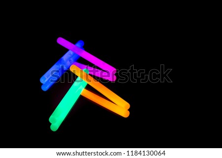 Colorful fluorescent light neon glow stick on mirror reflection black background. Blue pink orange green big glow sticks