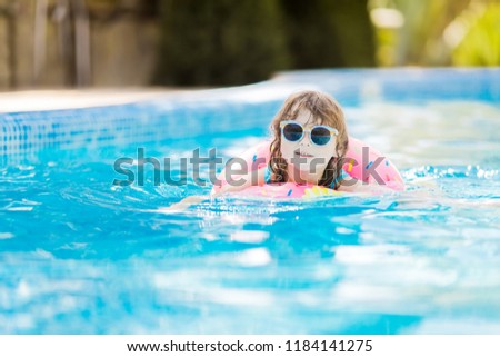 Little girl in swimming pool on funny inflatable donut float ring, learning how to swim.