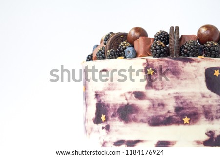Cake with white and black cream, decorated with blueberries, blackberry, chocolate chip cookies, candies, bars and  gold star on a white background. Picture for a menu or a confectionery catalog.