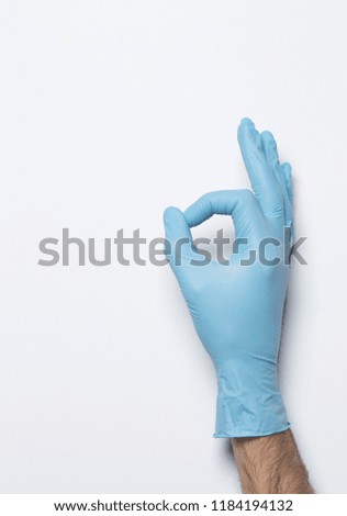 Blue latex medical gloves on a female hand, shows the character okay