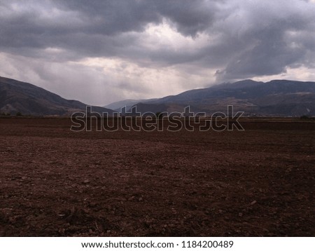 
cultivation of land, tree at medium distance, mountains at a great distance, sky with white clouds and black background, in the vicinity of the city of Cusco, Peru.