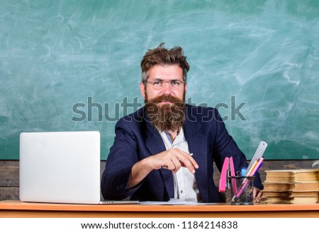 Teacher formal wear sit table classroom chalkboard background. Pay attention to details. Teacher concentrated bearded mature schoolmaster listening with attention. Teacher listening answer or report.