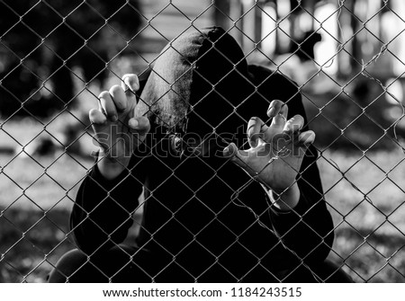 Young unidentifiable teenage boy holding the wired garden at the correctional institute in black and white, conceptual image of juvenile delinquency, focus on the boys hand. Royalty-Free Stock Photo #1184243515