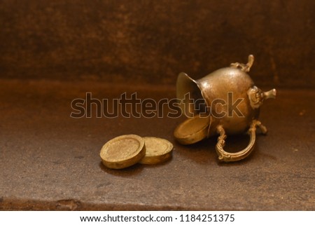Golden coins out off a little pot on a stone gorund under the natural light of the sun.