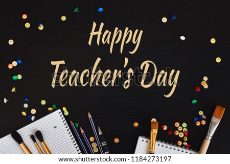 Happy Teachers' Day greeting card. Congratulation text and school supplies on black wooden background