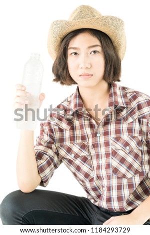 Young pretty woman in a cowboy hat and plaid shirt holding a water bottle isolated on white background