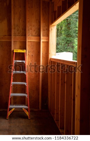 Ladder against a window in an empty interior of a house under construction, with exposed wood studs and framing