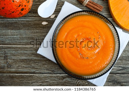 Delicate pumpkin puree in a black glass bowl on a wooden table. Top view.