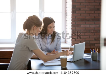 Female colleagues working together with laptop using corporate software in meeting room, office worker explaining coworker online task, discussing results or presenting new project on computer Royalty-Free Stock Photo #1184389300
