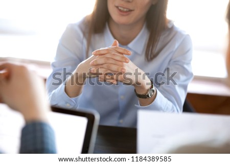 Smiling woman attentively listening to partners concentrated on business negotiations, nonverbal communication concept, focus on locked crossed fingers, clenched hands gesture close up view Royalty-Free Stock Photo #1184389585
