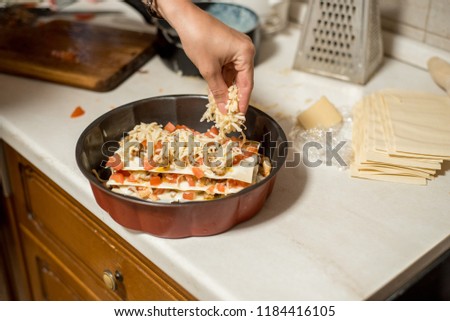 Woman cooking homemade classic lasagna bolognese, on dark blue table, with ingredients, top view copy space, hands in picture.