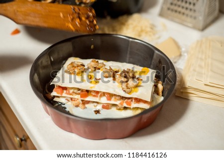 Woman cooking homemade classic lasagna bolognese, on dark blue table, with ingredients, top view copy space, hands in picture.