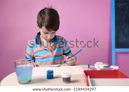 Caucasian boy spending time painting with colorful watercolors.