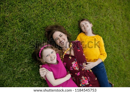 Mom and Two Daughters Laying on Ground Grass Being Silly Having Fun Laughing