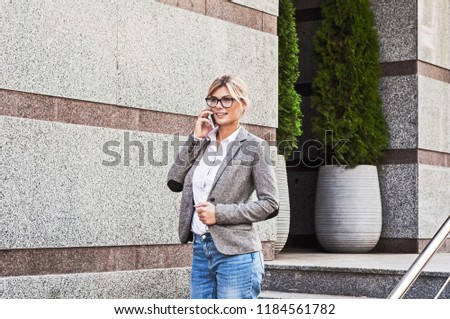 Business lady with mobile phone on the background of a gray building