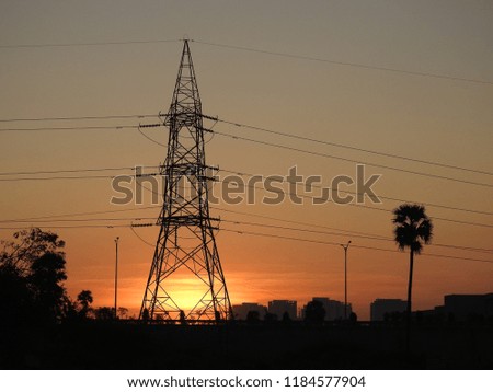 Early Morning Sunrise, orange color sky, sunlight through Big high voltage Electric Tower(pole), palm tree and other trees 