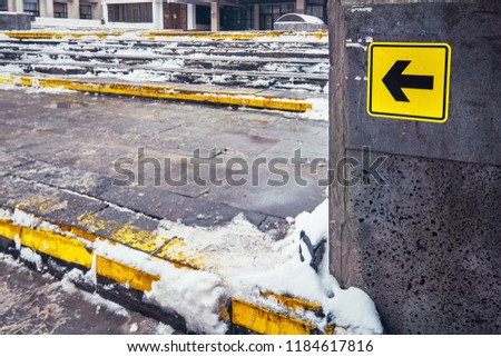 Yellow arrow for the disabled near high stairs in the street in winter in the snow