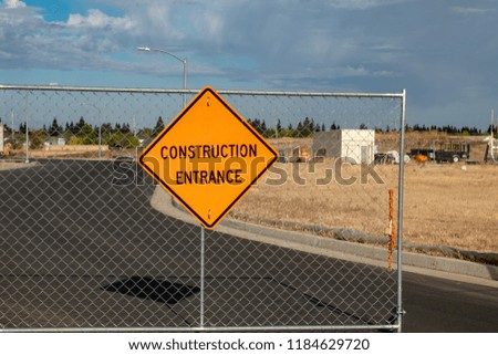 Orange construction entrance sign on a chain-link fence