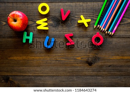 Elemerntary school concept. Letters of toy alphabet, apple and color pencils on dark wooden background top view copy space