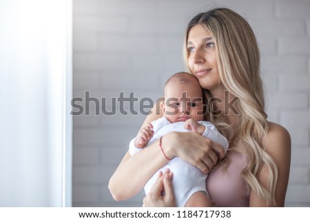 Newborn baby in a tender embrace of mother at the window