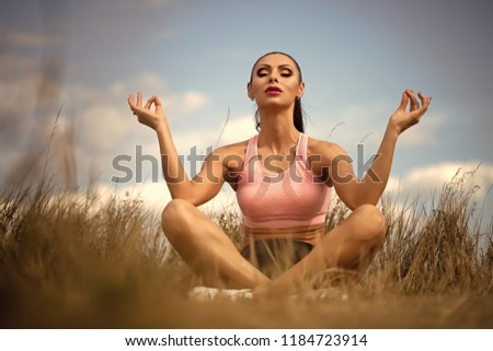 One pretty young brunette woman with straight beautiful body in sportswear sitting on grall having rest and making meditation while morning running outdoor on blue sky background, horizontal picture