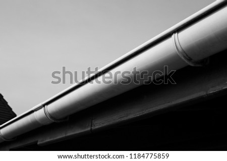 A black and white image of a plastic rain gutter.  This image can also be used to represent house maintenance. 