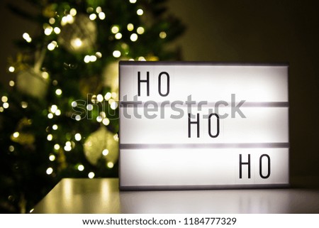 christmas concept - lihtbox with ho-ho-ho word in dark room with decorated christmas tree
