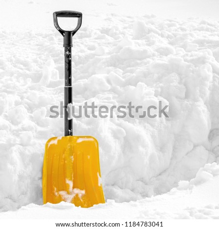 Yellow plastic shovel stuck upright in fluffy pile of white snow in winter. Picture with copy space on the right