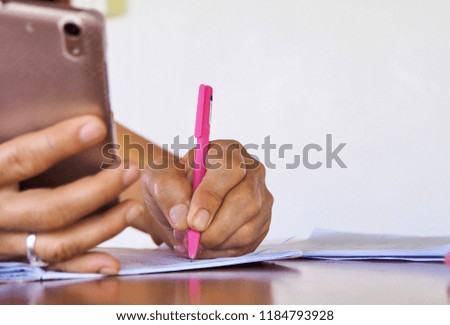 Woman is working or Writing a book And finding information using a smartphone. And access to the Internet by mobile phone.