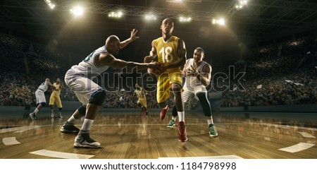 Basketball players on big professional arena during the game. Tense moment of the game. Male caucasian and black players fight for the ball