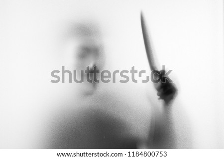 Shadow blur of horror man in fancy mask knife in his hand.Dangerous man behind the frosted glass.Mystery man.Halloween background.Black and white picture.Blur picture.