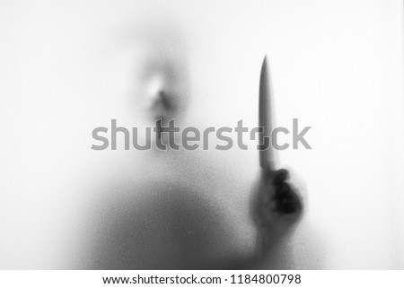 Shadow blur of horror man in fancy mask knife in his hand.Dangerous man behind the frosted glass.Mystery man.Halloween background.Black and white picture.Blur picture.