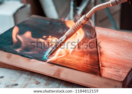 High quality wood planks and slabs, while being burnt with a brass, gas burner in woodshop in Italy. Details of the fire burst, and black wooden texture after the process.  Royalty-Free Stock Photo #1184812159