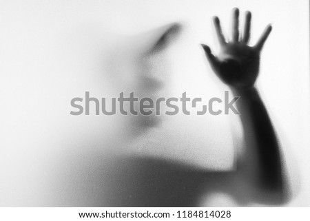 Shadow blur of horror man in fancy mask.Hands on the glass.Dangerous man behind the frosted glass.Mystery man.Halloween background.Black and white picture.Blur picture.